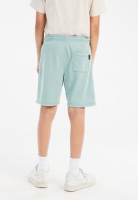 Mintgroene katoenen shorts met een elastische tailleband, zijzak en zichtbare stiksels, gedragen met witte sokken en sneakers.