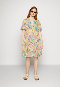Vestido com estampado floral, com mangas curtas e esvoaçantes, decote em V e silhueta em A. Fundo predominantemente azul com flores em rosa, amarelo e verde.
