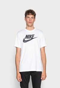 Hvit bomulls t-skjorte med en stor svart Nike-logo på forsiden. Korte ermer og rund hals. Denne t-skjorten har en avslappet passform og en glatt tekstur.