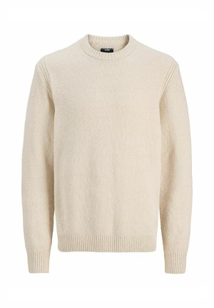 Pull en maille beige clair avec col côtelé, associé à un short en denim bleu clair. Porté avec des chaussettes grises et des baskets grises.
