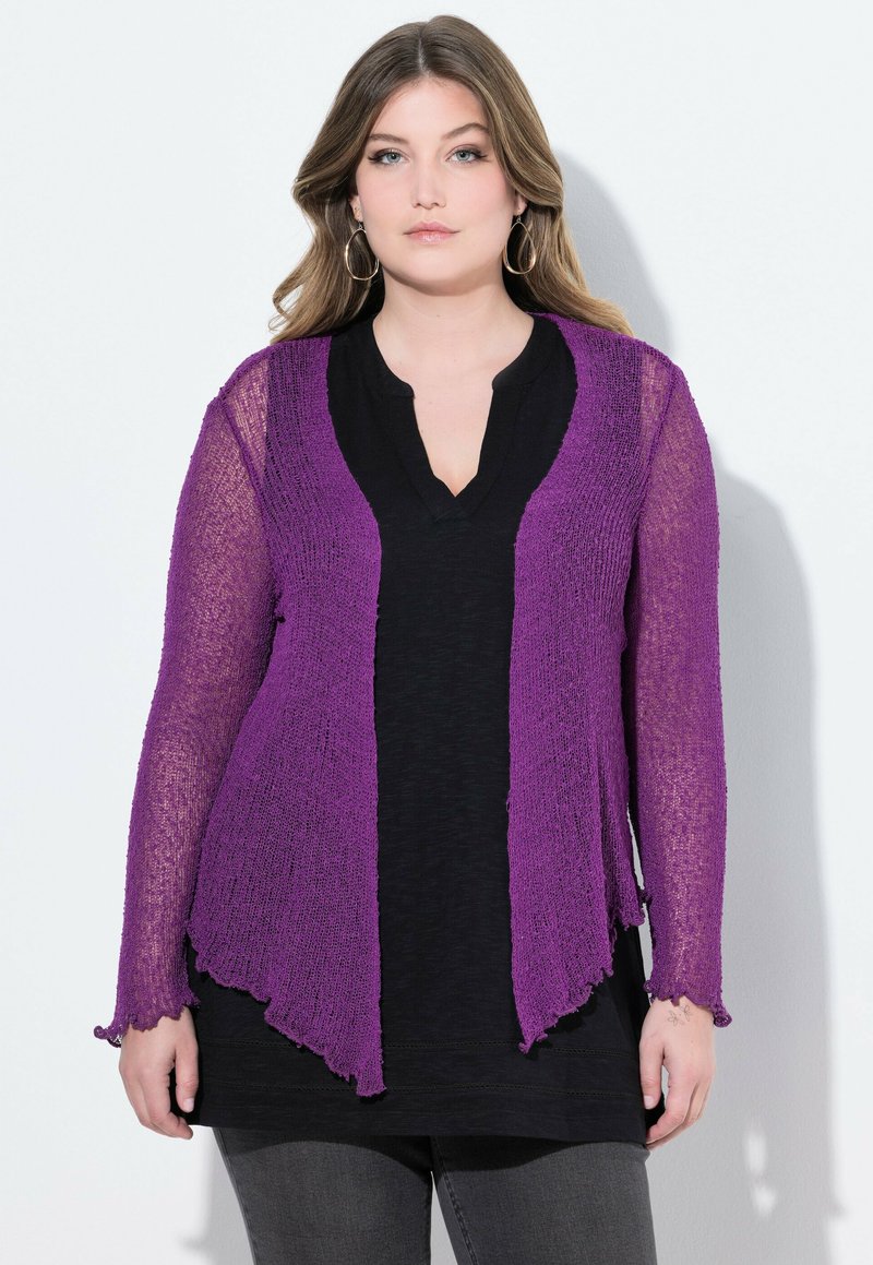 Lila stickad cardigan med öppen front, långa ärmar och en texturerad yta, bärs över en svart topp. Kanterna är vågiga.