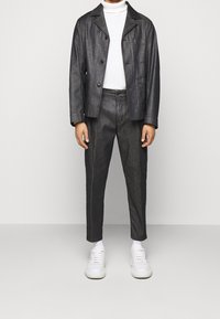 Chaqueta de mezclilla oscura con dos bolsillos frontales, jersey de cuello vuelto blanco y pantalones de mezclilla oscura a juego. Zapatillas blancas completan el atuendo.