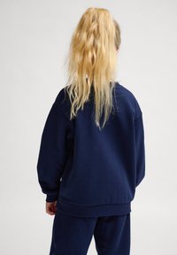 Marinblå sweatshirt med avslappnad passform, ribbade ärmslut och nedkant. Tyget verkar mjukt och hållbart; slät textur med en ren finish.