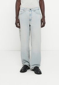 Világoskék farmernadrág laza szabással, oldalsó zsebfedéllel és finom kopással. Klasszikus gombos és cipzáras záródással rendelkezik.