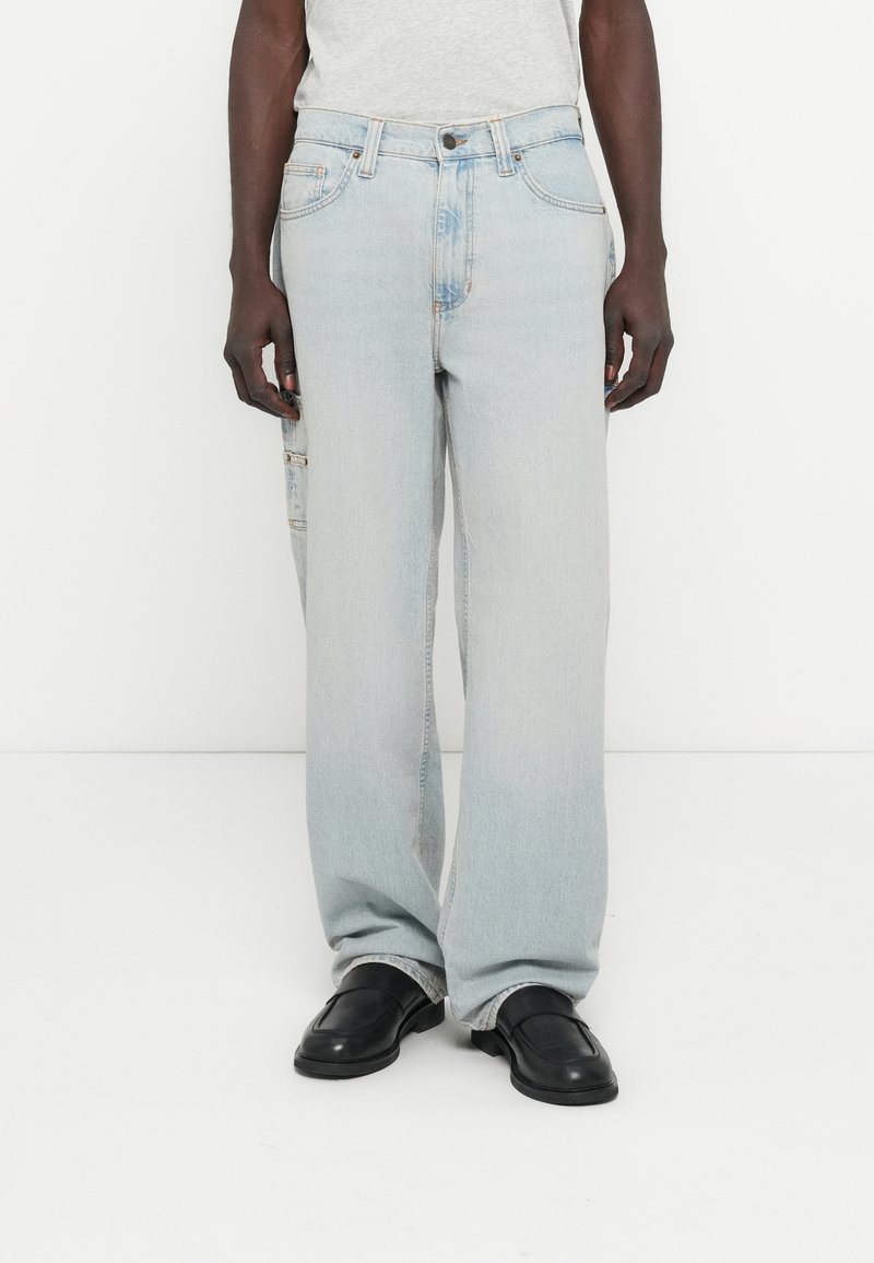 Világoskék farmernadrág laza szabással, oldalsó zsebfedéllel és finom kopással. Klasszikus gombos és cipzáras záródással rendelkezik.