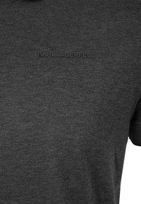 Camiseta de algodón gris oscuro con un logo en relieve negro y texturizado de "KARL LAGERFELD" en el pecho. Mangas cortas y un corte clásico.