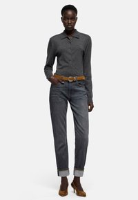 Szary sweter na guziki z długimi rękawami, zestawiony z podwiniętymi ciemnymi jeansami i brązowymi zamszowymi szpilkami, z paskiem ze skóry w kolorze brązowym.