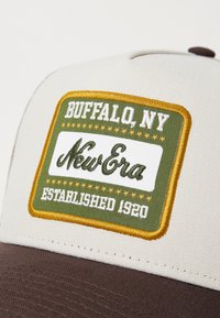 Podešiva kapa s krem prednjim dijelom, smešnim vizorom i izvezenom oznakom s natpisima "BUFFALO, NY," "New Era," i "ESTABLISHED 1920" u živopisnim bojama.