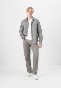 Gray and white striped button-up shirt over a white t-shirt, paired with light gray trousers and white sneakers, standing against a plain background.