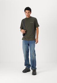 Cămașă din bumbac de culoare verde măslin, cu mâneci scurte și croială dreaptă. Asortată cu blugi de culoare albastru deschis și pantofi sport negri. Detalii de design simple.