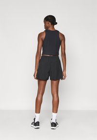 Svart cropped tank topp og svarte shorts. Shortsene har elastisk linning og en avslappet passform. Svarte treningssko med hvite detaljer.