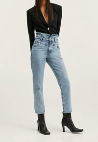 Schwarzer Blazer mit einem einzigen Knopf, kombiniert mit hochgeschnittenen, hellblauen Mom-Jeans und schwarzen Ankle Boots mit quadratischer Zehenform.