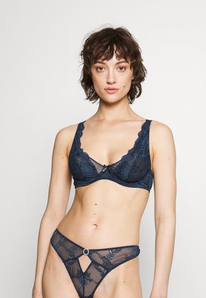 Navy kanten bh en bijpassende string, met bloemmotieven, doorschijnende panelen, golvende randen en een decoratieve ring op de string.