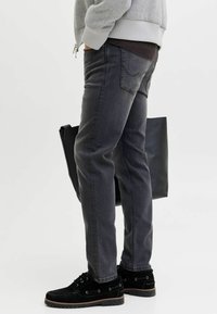 Dark gray jeans with a straight cut, featuring subtle stitching, side pockets, and a black tote bag being held. Accented with black shoes.