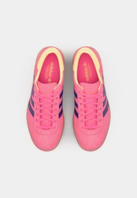 Roosa Adidas'i tossud, millel on lillad triibud, tekstureeritud pealmine osa ja kollased aktsendid vooderdisel. Kummist välistald ja paeltega disain.