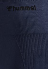 Gros plan d'un tissu texturé bleu marine avec le logo hummel noir et l'emblème stylisé d'abeille en haut au centre.