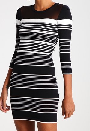 Robe rayée noire et blanche avec des manches trois quarts, encolure ronde et partie supérieure transparente. Coupe près du corps, texture côtelée.