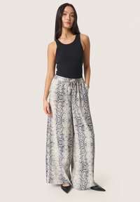 Zwarte geribbelde tanktop gecombineerd met losse, slangenprint houten broeken in crème en navy, voorzien van een elastische tailleband en zijzakken.