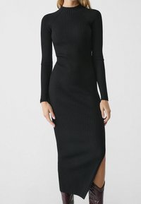 Abito in maglia nera a coste con maniche lunghe, colletto alto, design aderente e uno spacco laterale. Il tessuto ha una finitura texturizzata.