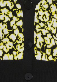 Cardigan noir avec un motif léopard jaune et blanc. Il présente un tricot texturé et cinq boutons noirs sur le devant.