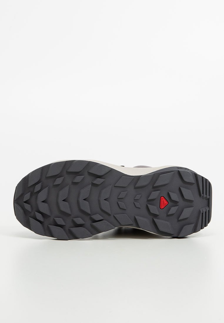 Podeszwa buta z wytrzymałą czarną gumą, z wielokierunkowym wzorem bieżnika i czerwonym akcentem w okolicy obcasa.