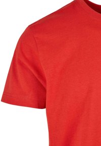 T-shirt rouge à manches courtes en coton montrant l'épaule, la manche et le haut de la poitrine avec des détails de couture visibles.