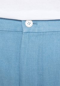 Ljusblå linbyxor har en mjuk yta, midjeband med knappstängning framtill och diskret sömdetalj.