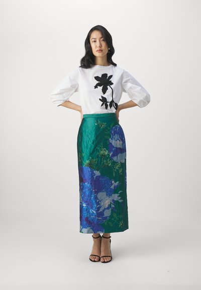 Vit blus med svart blommönster, kombinerad med en lång grön kjol med blå blommönster. Svarta sandaler med remmar fulländar outfiten.