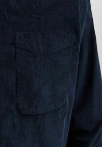 Tmavě modrá manšestrová košile s viditelnou náprsní kapsou, žebrovanou texturou a klasickým límečkem, zdůrazňující strukturovaný střih.