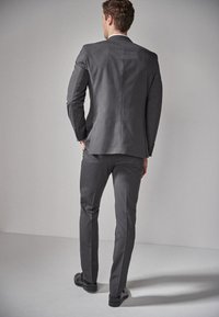 Veste de costume grise avec un pantalon assorti, design ajusté, texture lisse et subtil éclat, complétée par des chaussures noires élégantes.