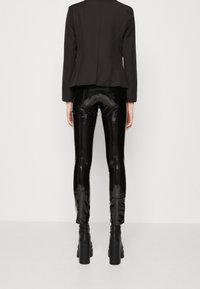 Svart figursydd blazer med en slät textur, tillsammans med högblanka svarta leggings. Kraftiga svarta platåklackar fulländar outfitten.