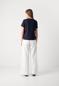 T-shirt en bleu marine à manches courtes avec un col rond, associé à un pantalon large blanc avec des ourlets et des poches latérales.