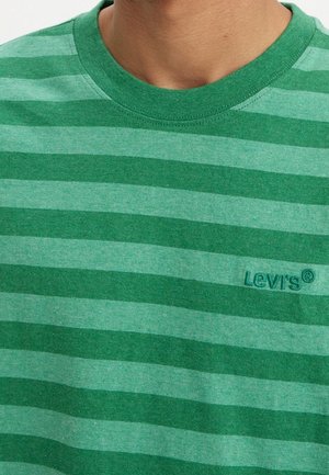 Mężczyzna noszący zieloną pasiastą koszulkę Levi's z okrągłym dekoltem, pokazując tylko górną część klatki piersiowej i szyi.