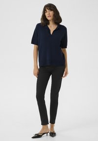 Marinblå kortärmad polo med V-ringning, kombinerad med svarta slim fit-byxor och svarta kitten heels med rosettdetalj.
