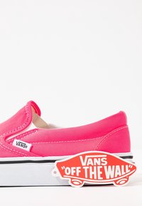 Chaussure Vans rose vif à enfiler avec semelle blanche et bande noire, montrant une petite étiquette Vans sur le côté et le logo rouge "Off The Wall" attaché près du talon.
