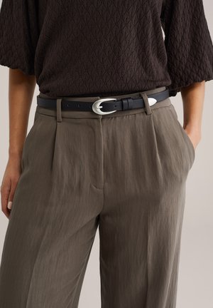 Crni kožni remen sa srebrnom kopčom nošen preko širokih, naboranih maslinasto zelenih hlača. Teksturirani tamnosmeđi top s uzorkom u obliku dijamanata.