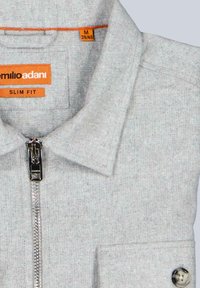 Grauer, taillierter Polo mit Reißverschluss, strukturierter Stoff und orangen Etiketten. Verfügt über einen Kragen und eine einzelne Brusttasche mit Knopfdetail.
