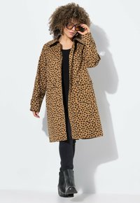 Bruine panterprint jas met een kraag, twee voorzakken en lange mouwen. Draag het over een zwarte top en combineer het met zwarte laarzen en strakke jeans.