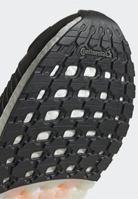 Gros plan d'une semelle de chaussure noire avec motif de grip texturé et logo Continental, montrant un matériau de rembourrage blanc sous la bande de roulement.