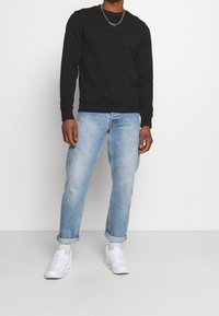 Sweat-shirt noir en mélange de coton, col rond, poignets et ourlet côtelés ; associé à un jean denim bleu clair retroussé et des baskets blanches.