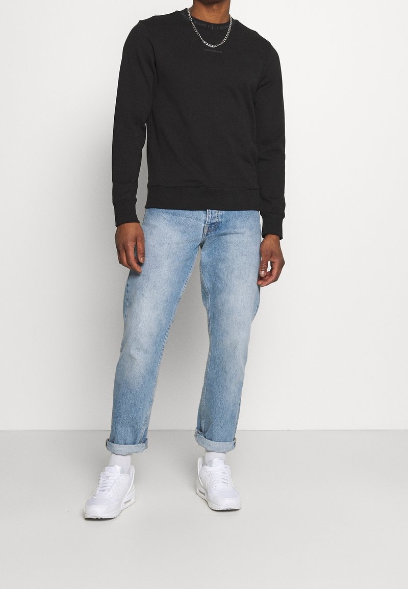 Sweat-shirt noir en mélange de coton, col rond, poignets et ourlet côtelés ; associé à un jean denim bleu clair retroussé et des baskets blanches.