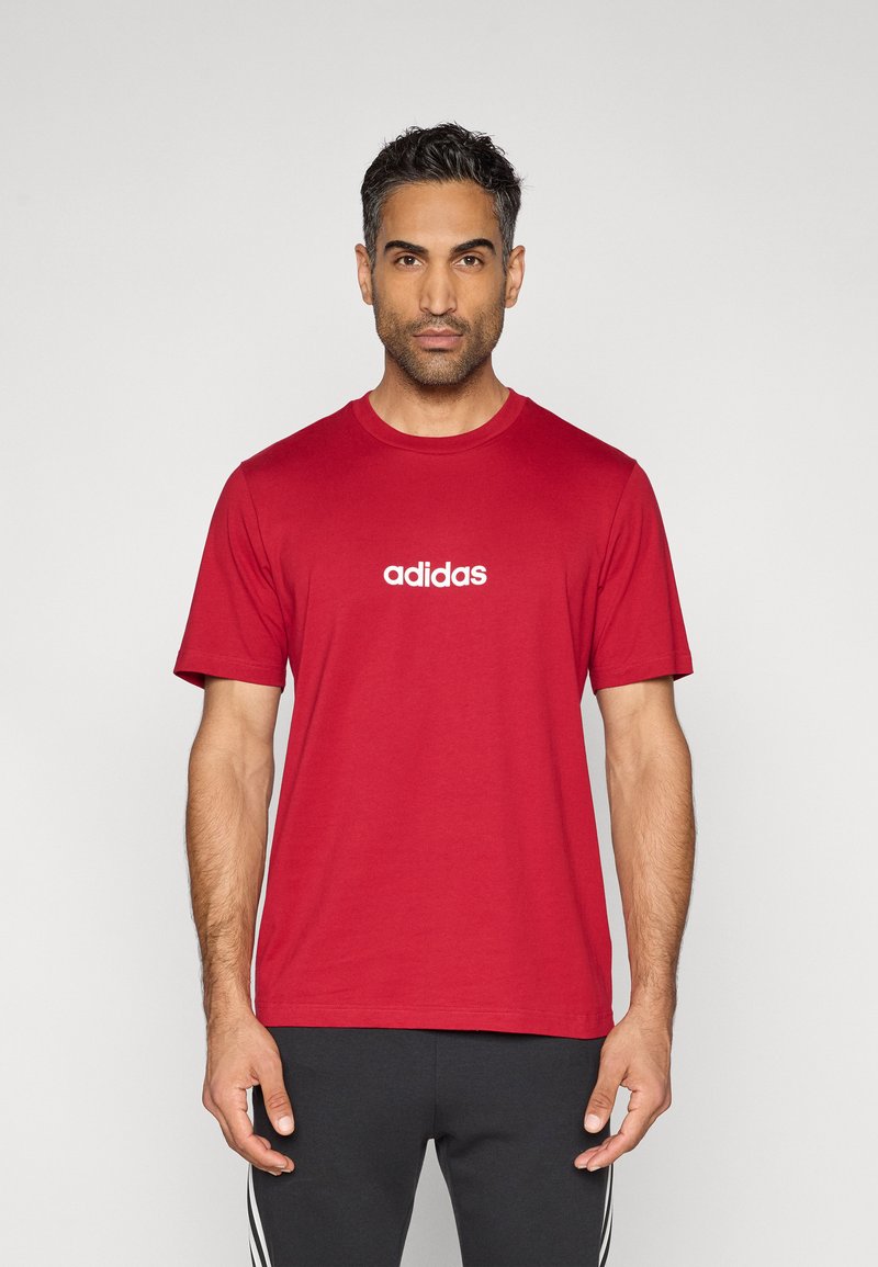 Punane puuvillane T-särk lühikeste varrukatega, ümar kaelus ja valge "adidas" logo rinnal keskendatud. Lihtne disain, sile tekstuur.