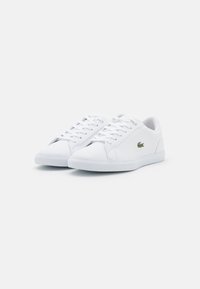 Sneakers bianchi in pelle con una texture liscia, dotati di un classico design con lacci e un piccolo logo verde sul lato.