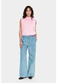 Top senza maniche di un leggero rosa pallido con scollatura arricciata abbinato a pantaloni larghi in denim blu chiaro. L'outfit presenta una vestibilità rilassata e tasche laterali.
