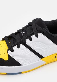 Czarno-żółty sneaker z teksturowaną białą panelem, posiadający czarne sznurówki, gumową podeszwę i uniesioną emblemat.