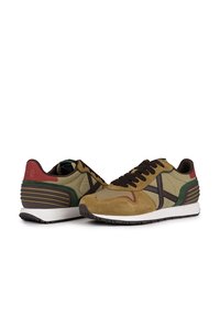 Zapatillas de material mixto en verde, marrón y rojo, con parte superior de ante y tela, cordones negros y suelas texturizadas. Diseño atlético clásico.