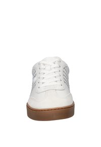 Zapatilla blanca con una parte superior de cuero liso, cordones planos, acentos de malla en los laterales y una suela de goma marrón. Punta redondeada y detalles de costura.
