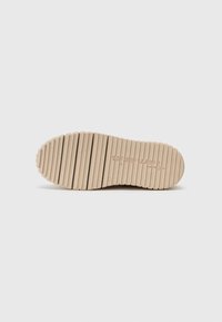 Beige gummisåle med vertikale spor og avrundede kanter, med et preget logo og teksturert overflate for bedre grep.