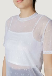 Camiseta de malla blanca con un sutil patrón A|X, escote redondo, mangas cortas y un diseño en capas para una apariencia ligera.