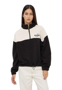 Pullover in pile nero e crema con colletto alto, mezza zip e orlo elasticizzato. Caratterizzato dal logo "WILDERNESS" in nero sul petto.